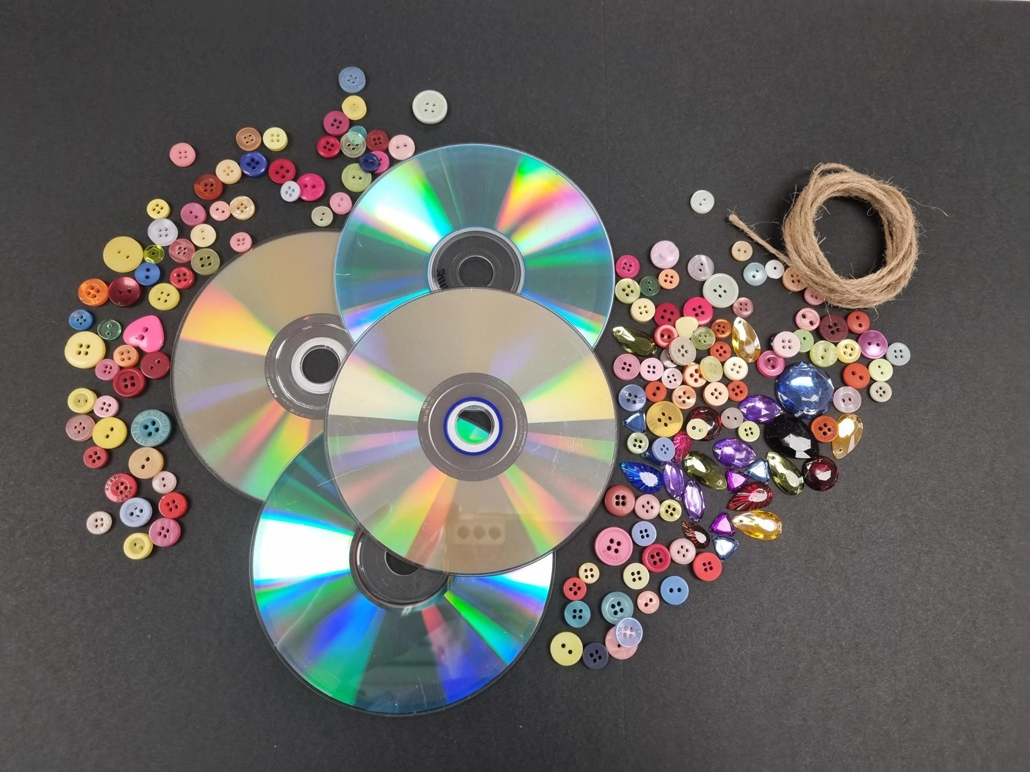 Four CD Discs, a range of multi-coloured buttons, gems and string layed out on a table